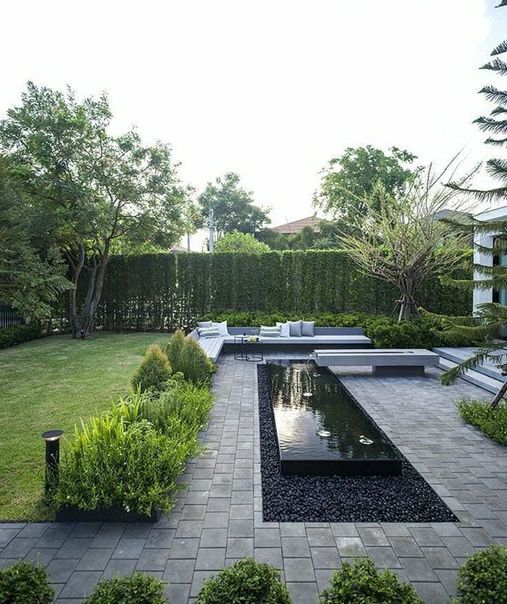 a modern garden with a green lawn, some shrubs, trees, a water body and modern outdoor furniture