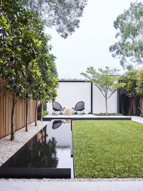 a modern garden with a green lawn, trees, a long pool, a deck with modern furniture is a cool and fresh space to be in