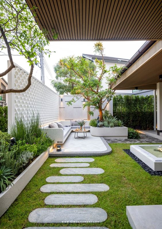a modern garden with a lovely terrace, a green lawn, a big tree and some grasses and greenery around is pure chic
