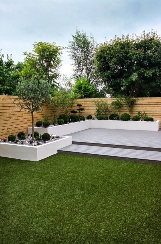 a modern garden with a two-level deck, a grene lawn and raised garden beds with trees and shrubs is wow