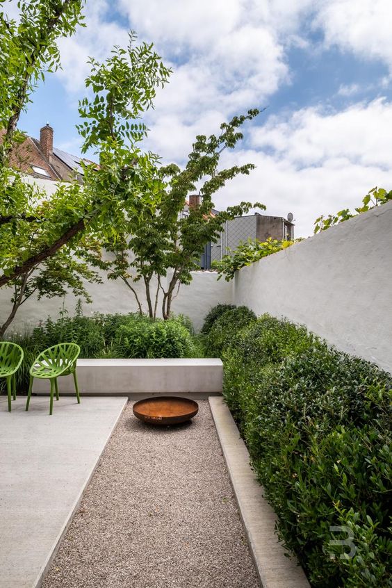 a modern garden with shrubs, trees and a fire pit plus a couple of green chairs is a cool and chic space