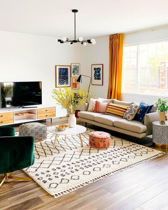 a modern living room with a boho rug, a neutral sofa with colorful pillows, a green chair, a gallery wall and bright mellow yellow curtains