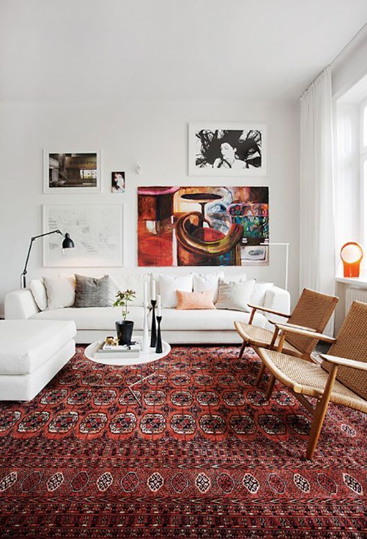 a modern living room with a boho rug, a white sofa and ottoman, cane chairs, a bold gallery wall and a black lamp