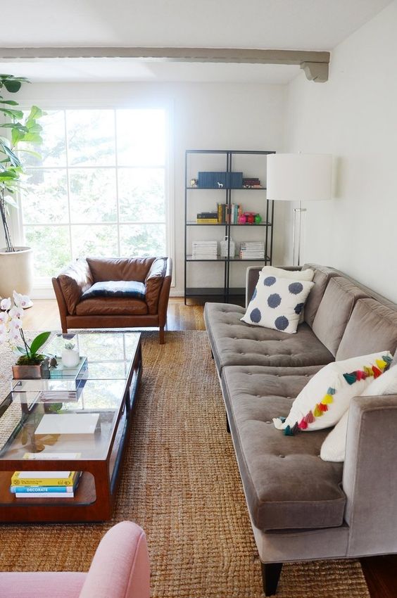 a modern living room with a grey sofa, an amber leather and a pink chair, a coffee table, some greenery and a shelving unit