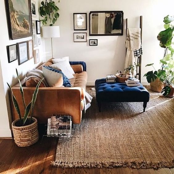 a modern living room with a jute rug, a beige sofa with pillows, a navy ottoman, some gallery walls and greenery