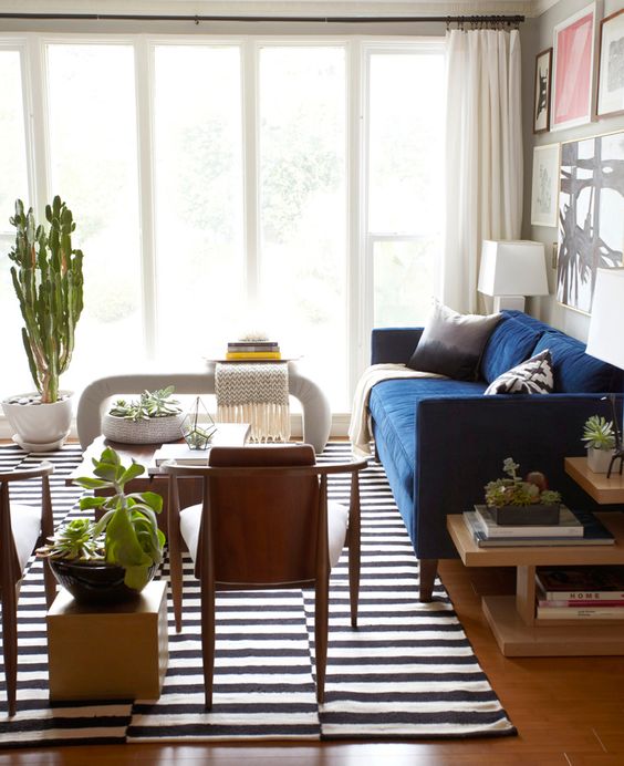 a modern living room with a navy sofa, a chair, potted plants, a creative console table and a gallery wall