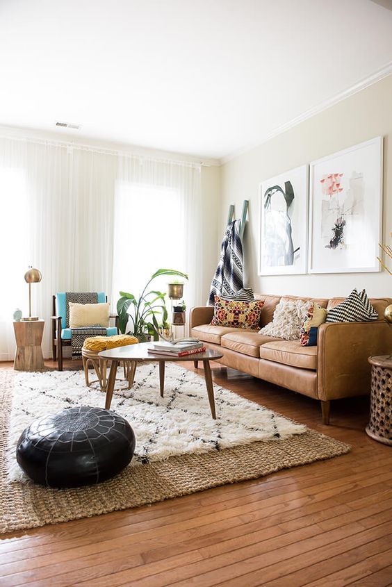 a modern living room with a tan leather couch, some chairs, a coffee table, layered rugs including a jute one, some chic decor