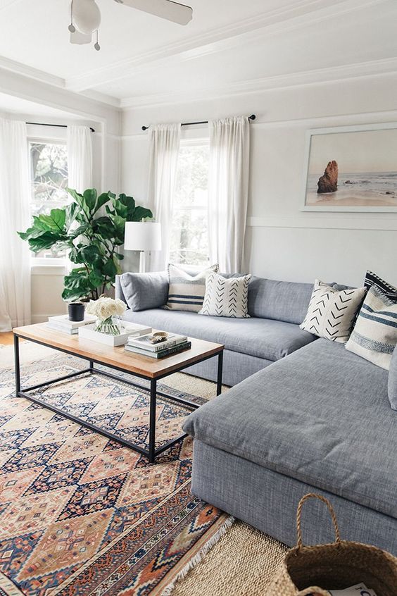 a modern living room with layered rugs, a boho one, a grey sectional, a coffee table and some printed pillows