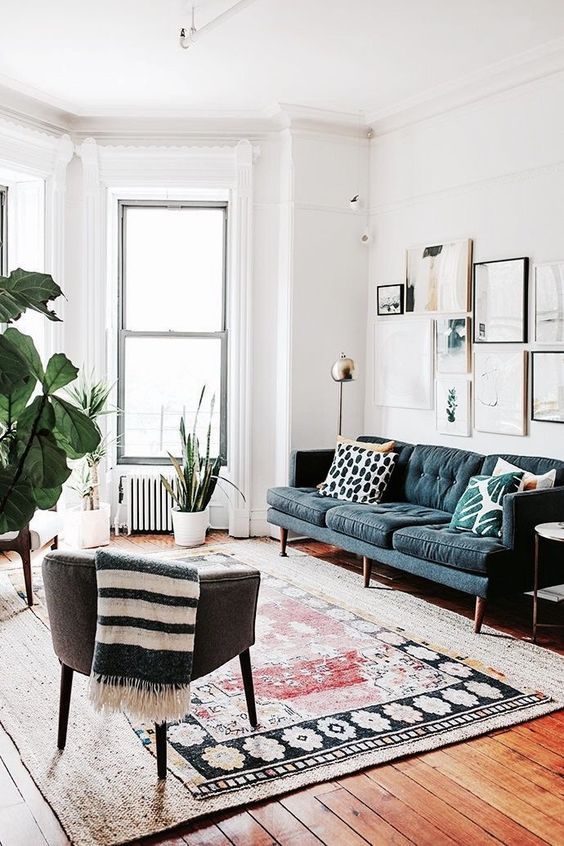 a modern living room with layered rugs, a grey chair, a navy sofa, a gallery wall and some potted plants is cool