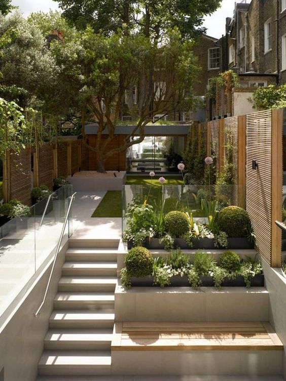 a modern multi-level garden with a green lawn, some blooms and a tree, a ladder, some built-in garden beds and a bench