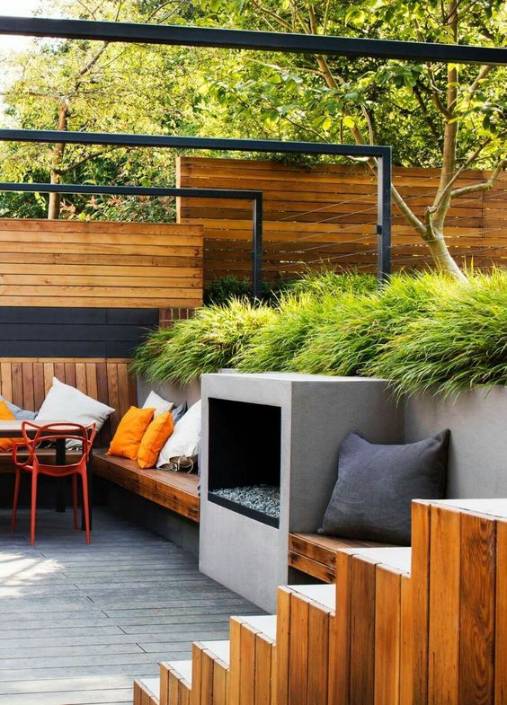 a modern multi-level outdoor space with a garden with grasses, stained built-in furniture, a fireplace and a ladder plus some pillows