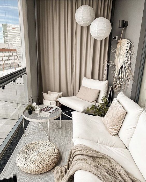 a modern neutral balcony with neutral upholstered furniture, a coffee table, a jute pouf and some fronds for a boho touch