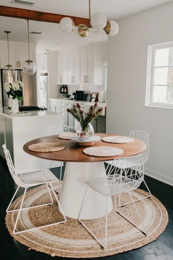 a modern neutral dining space with a jute rug, a round table, white metal chairs, a modern chandelier is a lovely and cozy nook