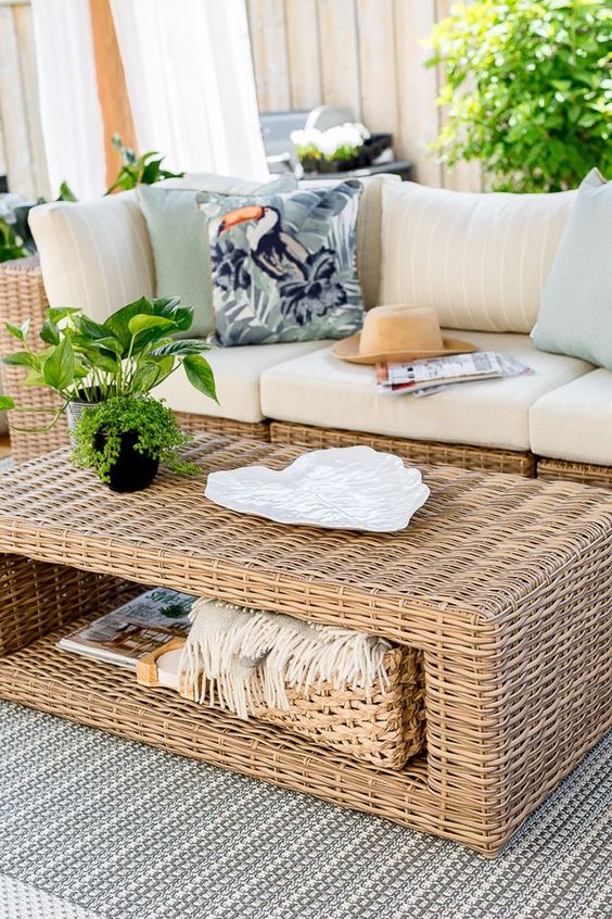 a modern neutral outdoor space with a wicker sofa and a matching coffee table, some greenery and pillows