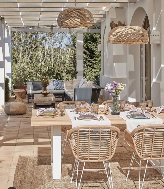 a modern outdoor dining area with a stained table, rattan chairs, woven pendant lamps and some blooms is lovely
