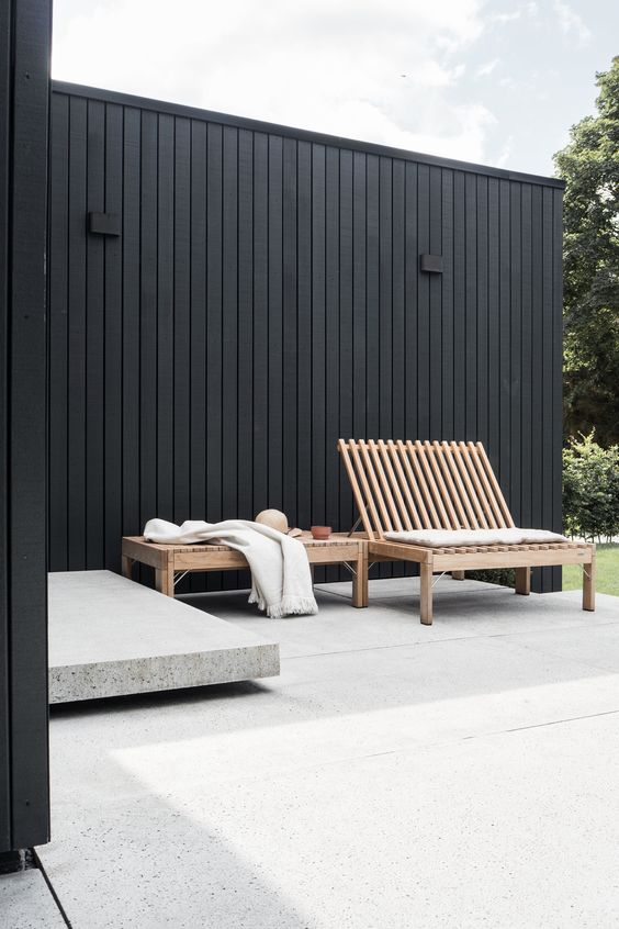 a modern outdoor space with a matte black fence and staiend furniture, a stone piece is a cool space to be in