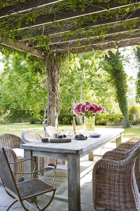 a modern rustic dining space with a reclaimed wood table and wicker chairs, a roof with vines over the space
