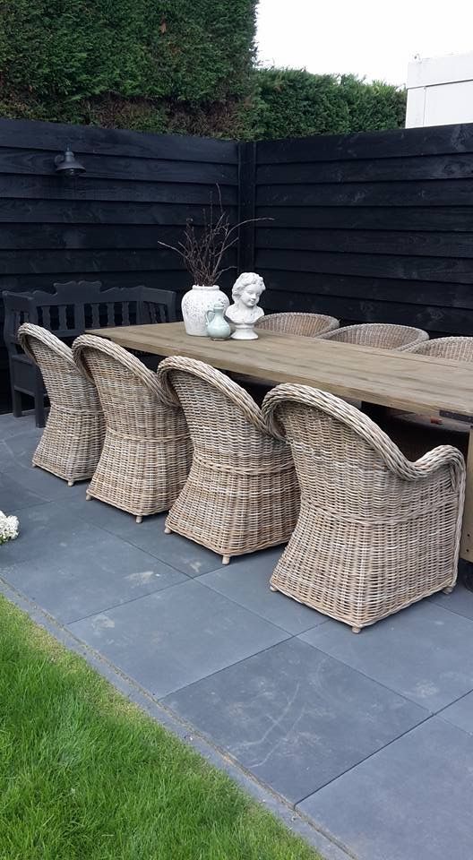 a modern rustic outdoor dining space with a stained table and wicker chairs plus a black bench is a cool space