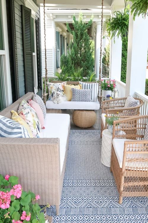 a modern rustic porch with wicker furniture, chairs, printed pillows, a rug and some greenery and blooms