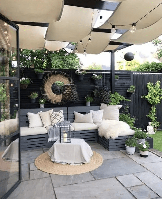 a modern terrace with a black fence, a graphite grey sofa with pillows, a coffee table, potted greenery and blooms