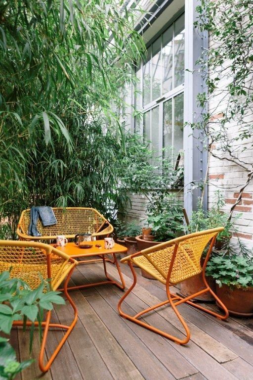 a modern terrace with a lot of greenery and potted plants, orange metal chairs, a loveseat and a table is amazing
