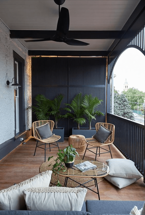 a modern terrace with black wooden slabs, wicker furniture, grey and neutral upholstery and potted greenery