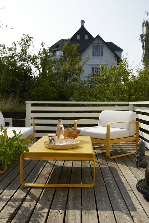 a modern terrace with stylish yellow chairs with white upholstery, a yellow coffee table and some greenery is super chic