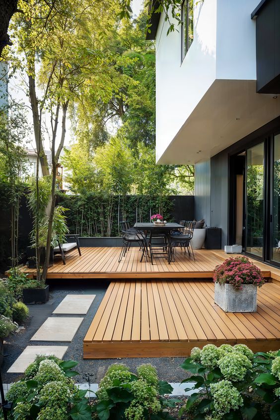 a multi-level deck with modern outdoor furniture, greenery, trees and blooms around is a cool outdoor space