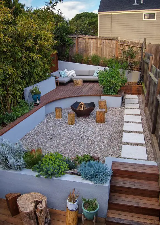 a multi-level deck with some plants, a gravel part with a fire pit and a sitting zone with trees and greenery