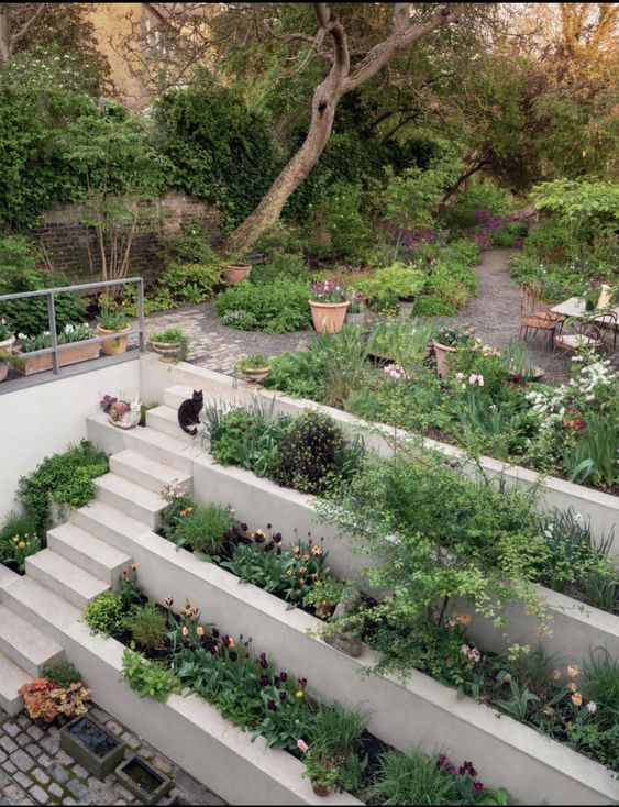 a multi-level garden with trees, greenery and blooms and a multi-tiered raised garden bed is a super cool space