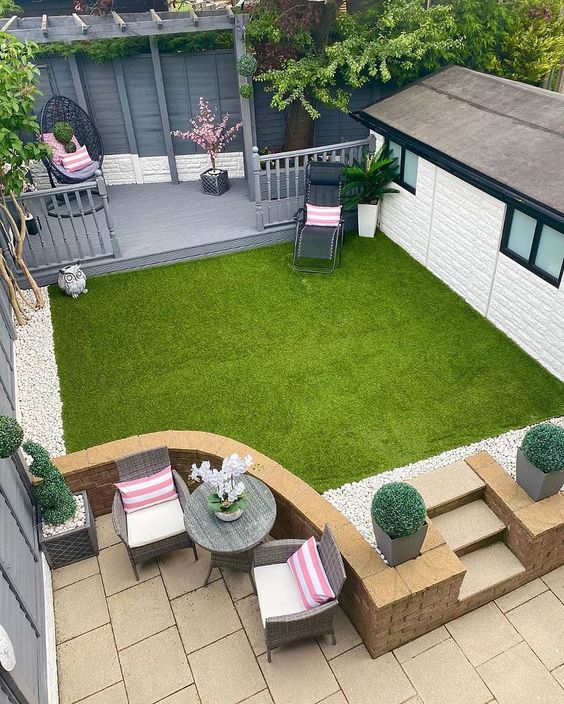 a multi-level outdoor space with an egg chair, a green lawn, a small dining zone and some plants