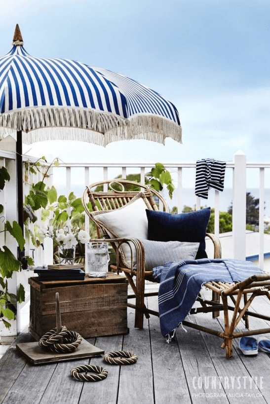 a nautical terrace with a rattan lounger and a wooden chest, an umbrella, some nautical textiles and greenery to refresh the space