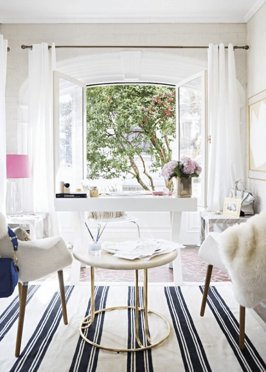 a neutral home office wiht a chic white desk, white chairs and a coffee table, pink touches and a cool view of the garden