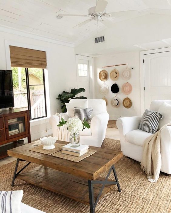 a neutral living room with a jute rug, white seating furniture, printed pillows, a hat hanger, a TV unit, some blooms and decor