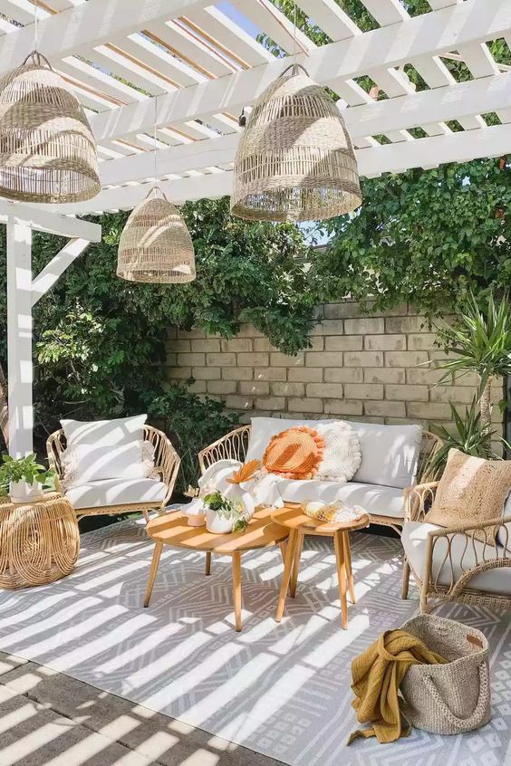 a neutral terrace with rattan furniture, a printed rug, pillows, woven lamps and some greenery