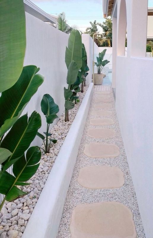 a perfect white fence paired with a long garden bed, tropical plants and neutral pebbles are a great idea for a tropical space