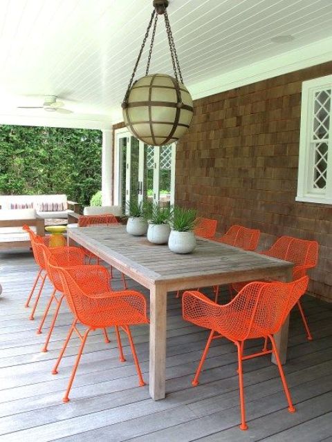 a porch dining space with a stained table, neon orange chairs, a sphere pendant lamp is a cool and bright space
