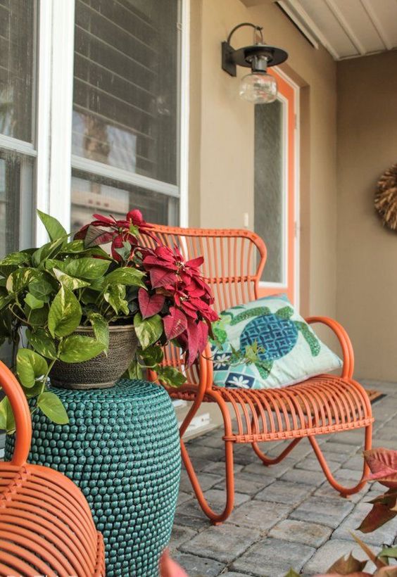a porch with bright orange wicker chairs, a teal side table and potted plants is a lovely and bright space