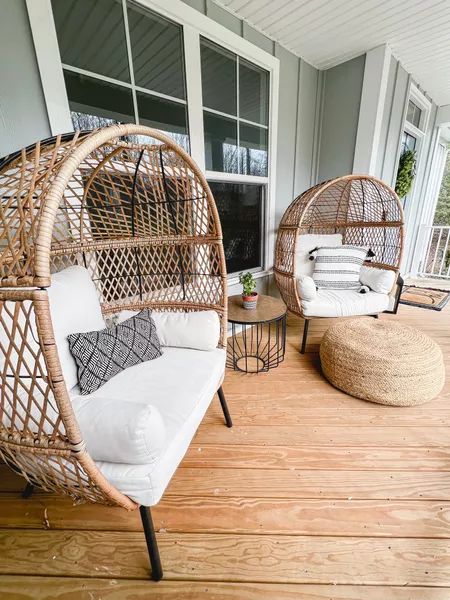 a porch with rattan chairs and neutral pillows, a jute pouf and a coffee table is a cool space to have some rest in
