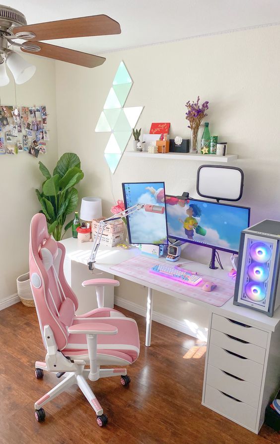 a pretty gaming desk setup with a desk, a pink chair, a PC, a shelf and decor and a statement plant