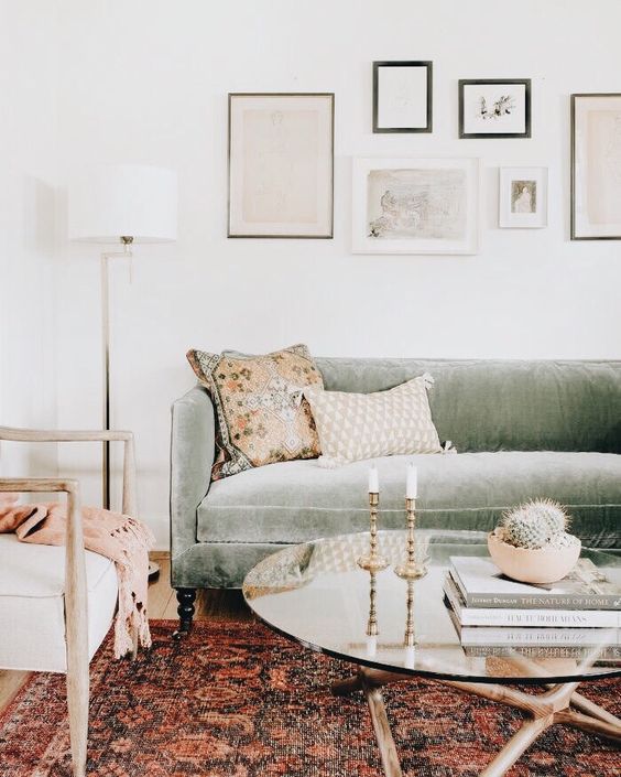 a pretty living room with a sage sofa, a neutral chair, a bold boho rug, a gallery wall and a glass coffee table with decor