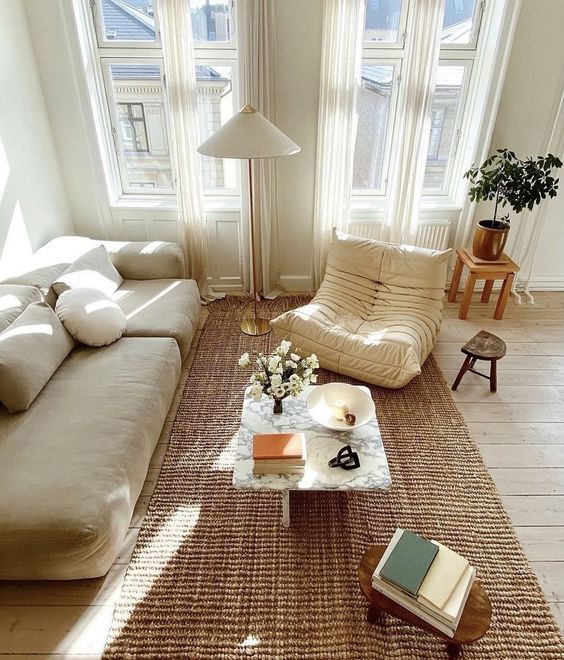 a pretty modern living room with a neutral sofa and a chair, a jute rug, chic coffee tables and blooms and greenery