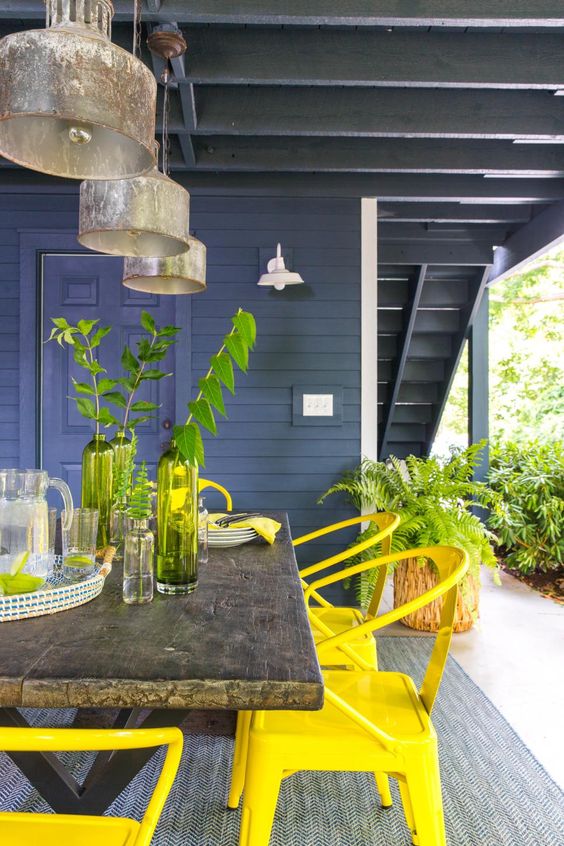 a pretty modern terrace with a reclaimed stained table, yellow chairs, metal pendant lamps and some greenery