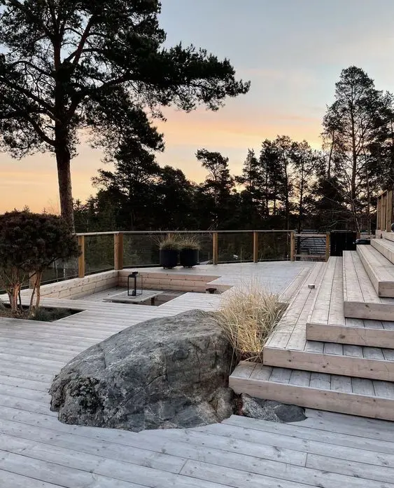 a pretty multi-level outdoor space with a bleached deck, some steps, a sunken conversation pit, rocks and trees