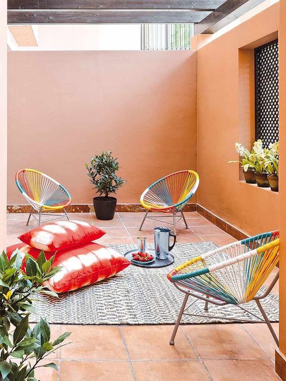 a pretty outdoor space with peachy walls, colorful chairs, coral pillows, a rug and some potted plants