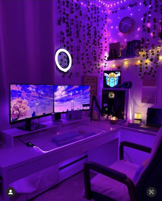 a purple gaming desk setup with a desk and two screens, a chair, some purple lights and greenery