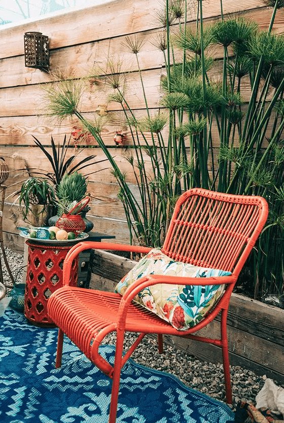 a red rattan chair with a colorful pillow and a bold rug, some potted plants for a colorful outdoor space