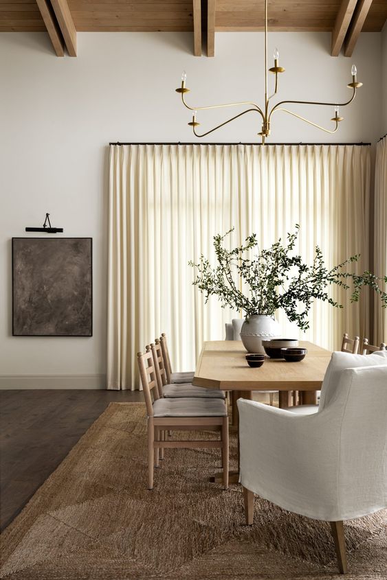 a refined modern dining room with a jute rug, a stained table, neutral chairs, a chandelier and some chic and cool decor