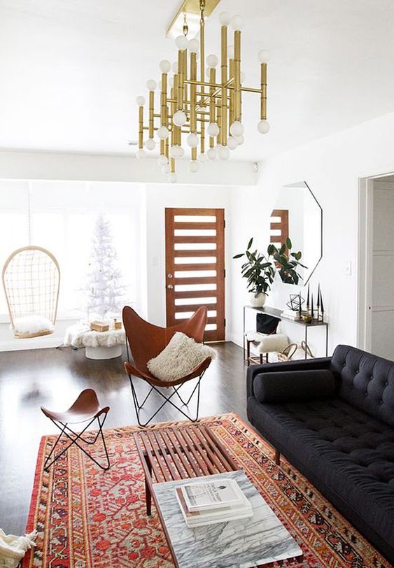 a refined modern living room with a bold boho rug, a black sofa, leather chairs, a pendant lamp, a console table with some decor