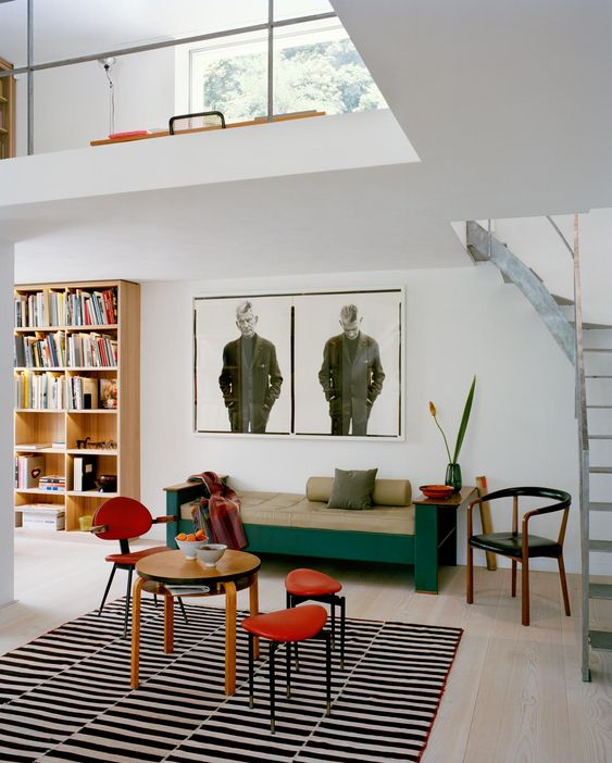 a refined modern living room with a bookcase, a daybed, a table with a chair and stool and a photo on the wall